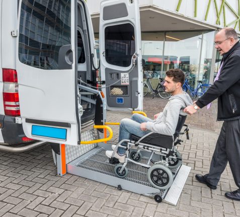 Taxi Driver Assisting Man On Wheelchair To Board Van